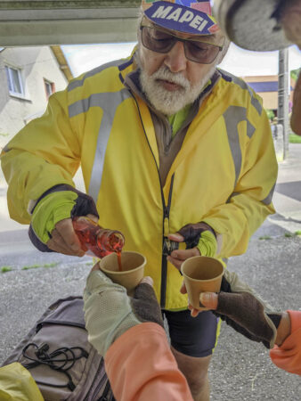 A Moncel-sur-Vaire, près de la salle communale où il y a 40 ans a eu lieu le repas de noce de nos amis, Gérard sert un verre dont un sirop de coquelicot très apprécié par Anne-Marie (MLC)